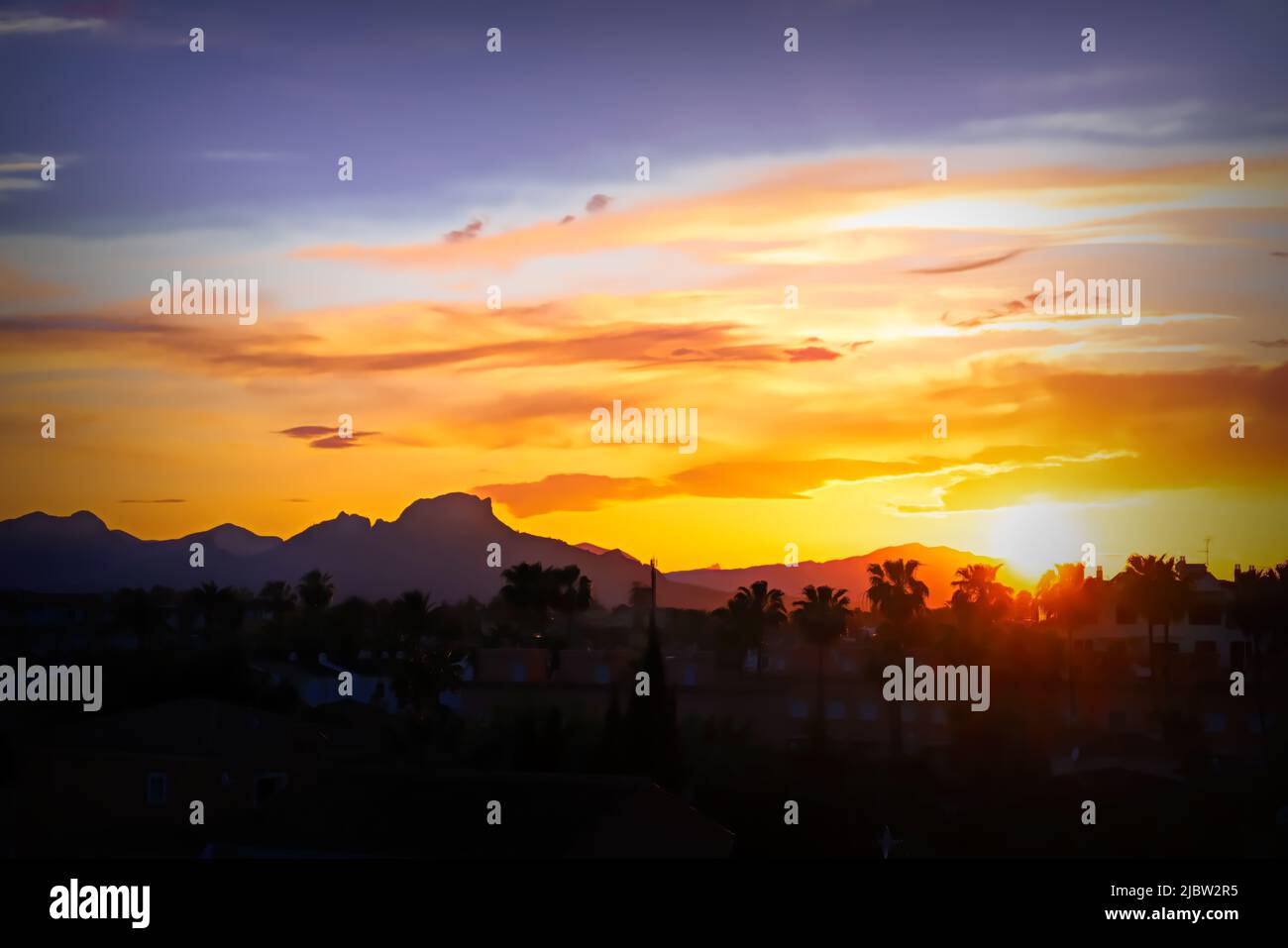 Denia Spain sunset with palm trees bright colourful sky and view to mountains Stock Photo