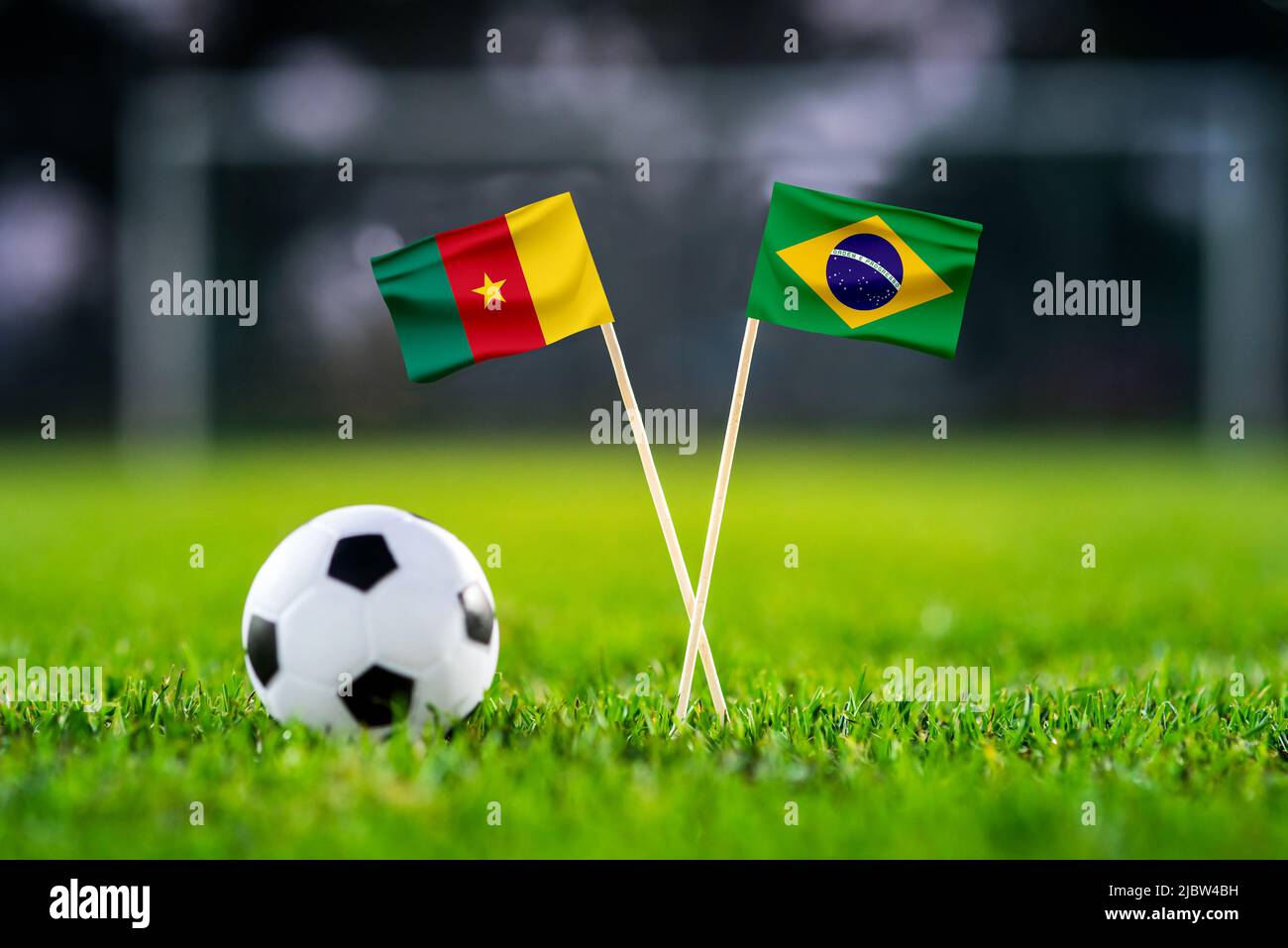 Cameroon vs. Brazil, Lusail, Football match wallpaper, Handmade national flags and soccer ball on green grass. Football stadium in background. Black e Stock Photo