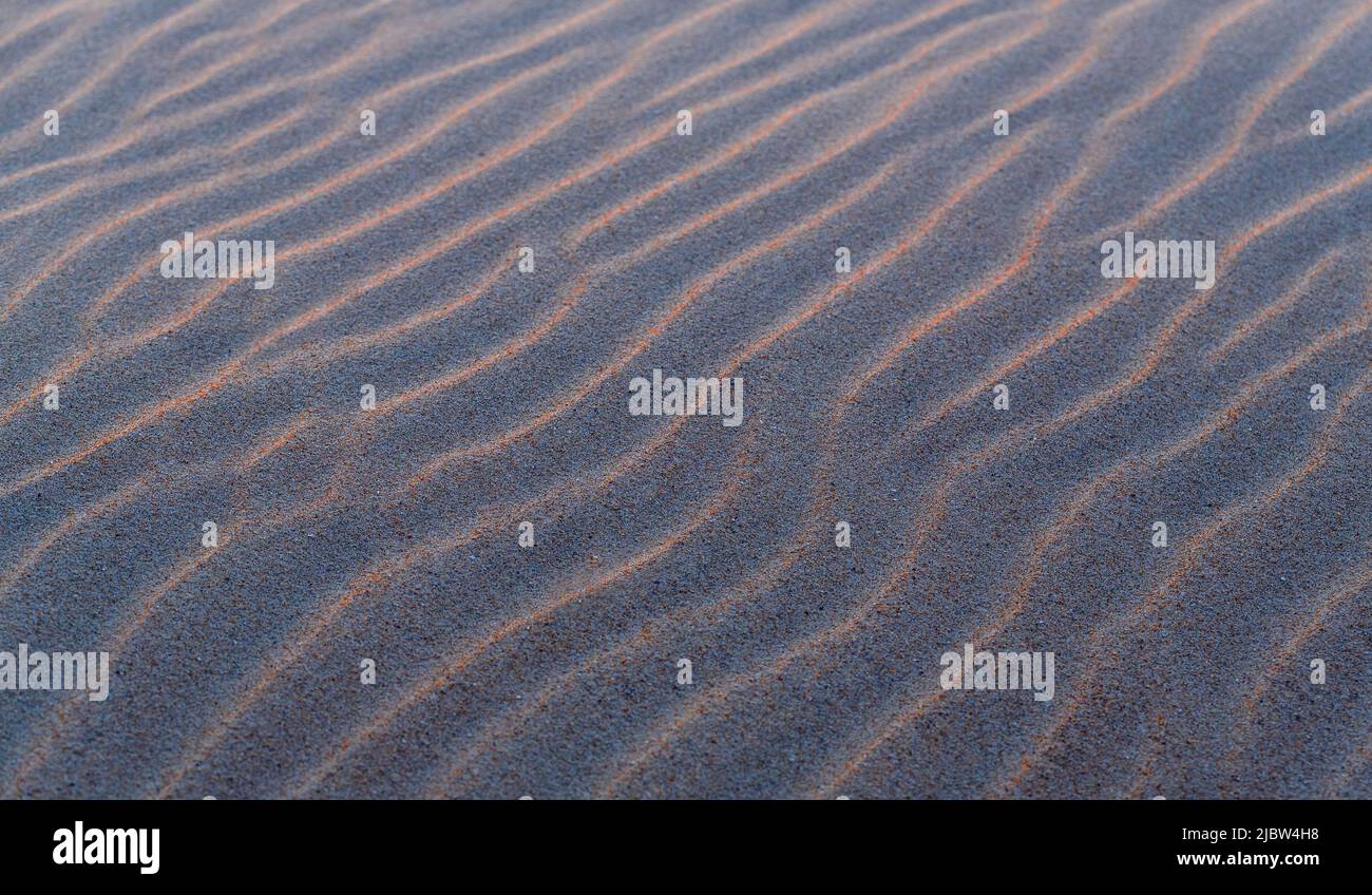 Sand ripples texture with waves at sunset as background or wallpaper. Stock Photo