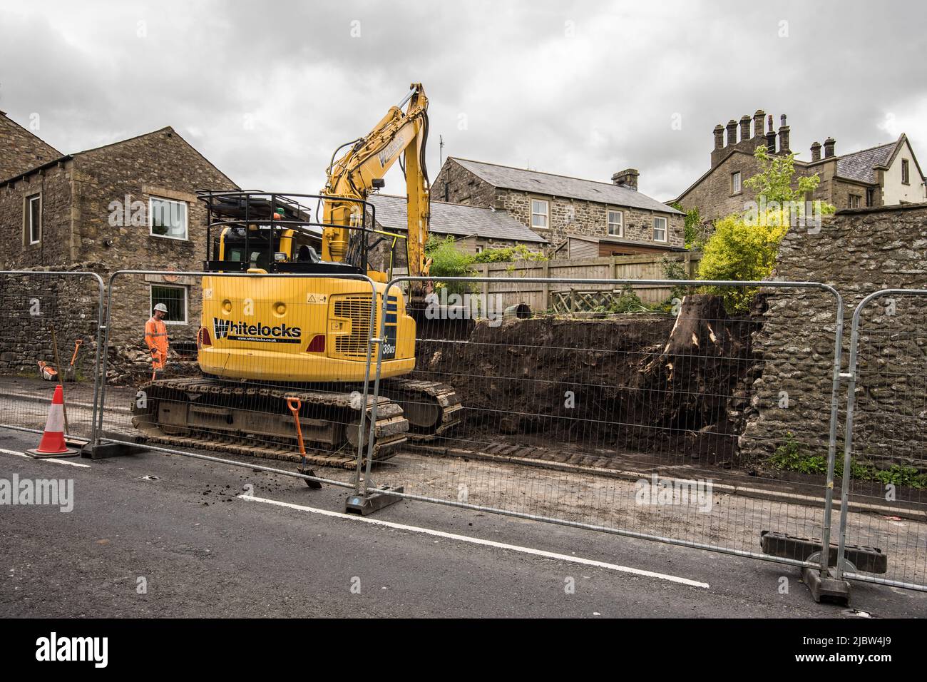 Work continuing on 9th June 2022 cutting back into the garden soil. Wall repair necessitating closure of one lane of A65 through village Long Preston. Stock Photo