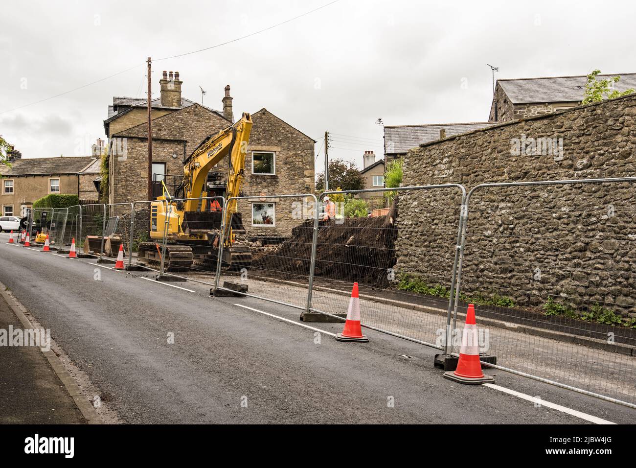 Work continuing on 9th June 2022 cutting back into the garden soil. Wall repair necessitating closure of one lane of A65 through village Long Preston. Stock Photo