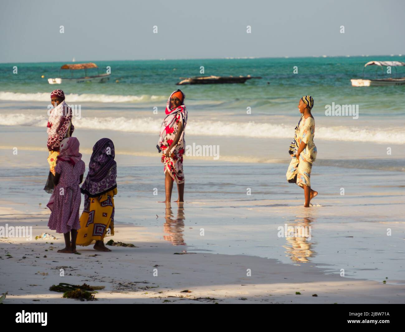 Matemwe, Zanzibar - Jan, 2021: Women in colorful clothes and headscarves. The daily life of the local people on the sandy beach of Zanzibar. Tanzania, Stock Photo