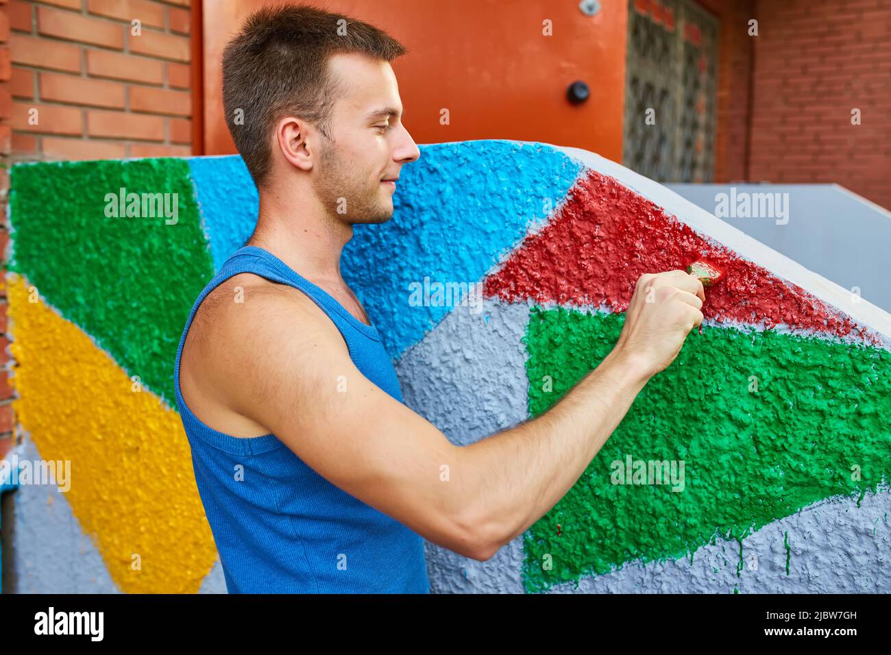 The guy paints the wall with a brush in bright colors, on the street