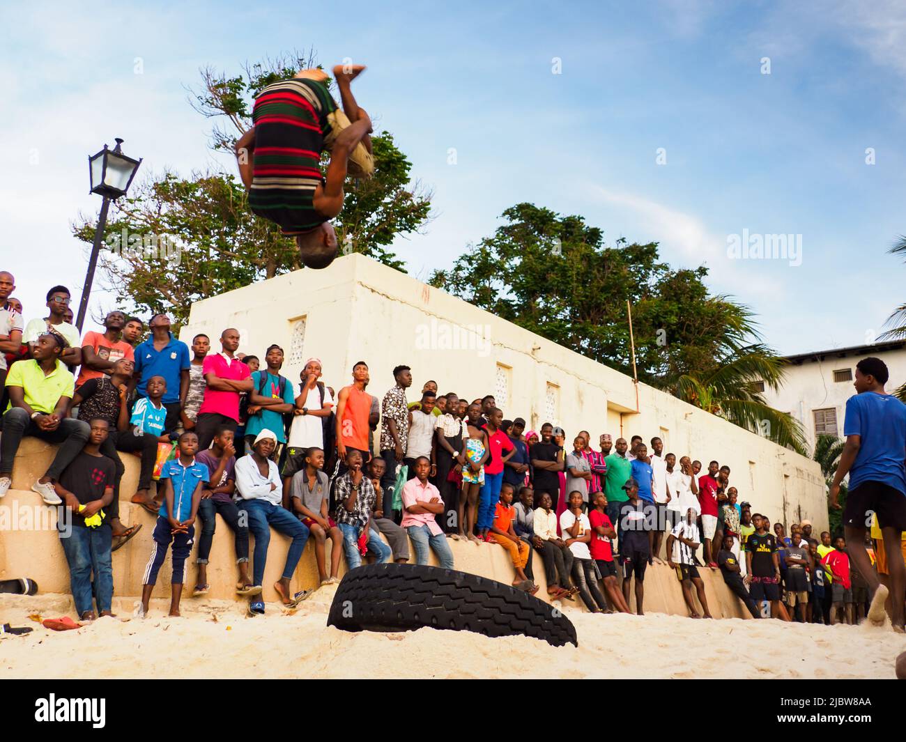 stone town zanzibar tanzania january 2021 crowds of people watch like young people jump on an inner tube on a sandy beach in stone town africa 2JBW8AA