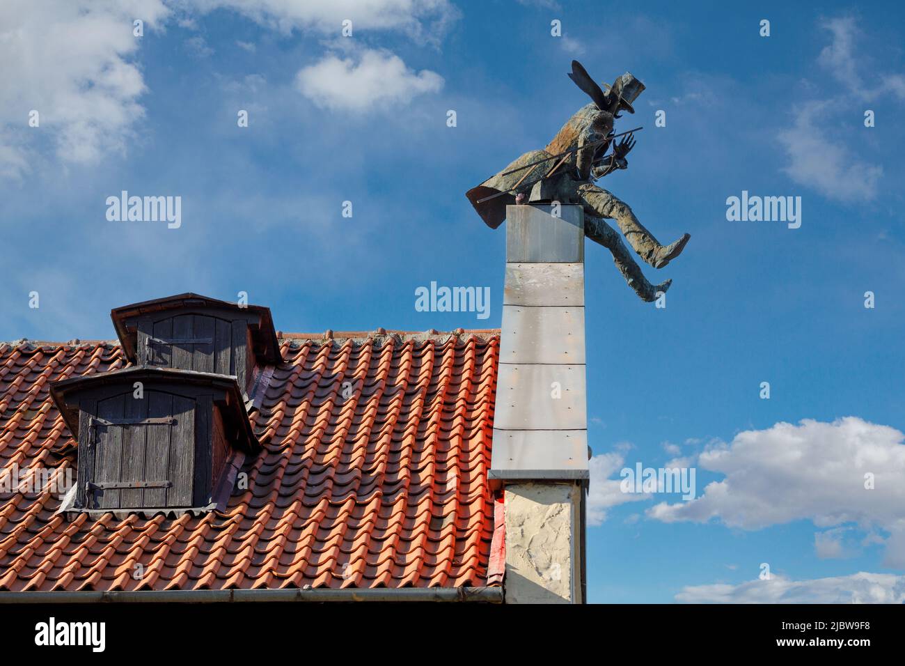 The chimney sweep on roof of house of Klaipeda in Lithuania. Red tiled roof and blue sky with white clouds in the background. Stock Photo