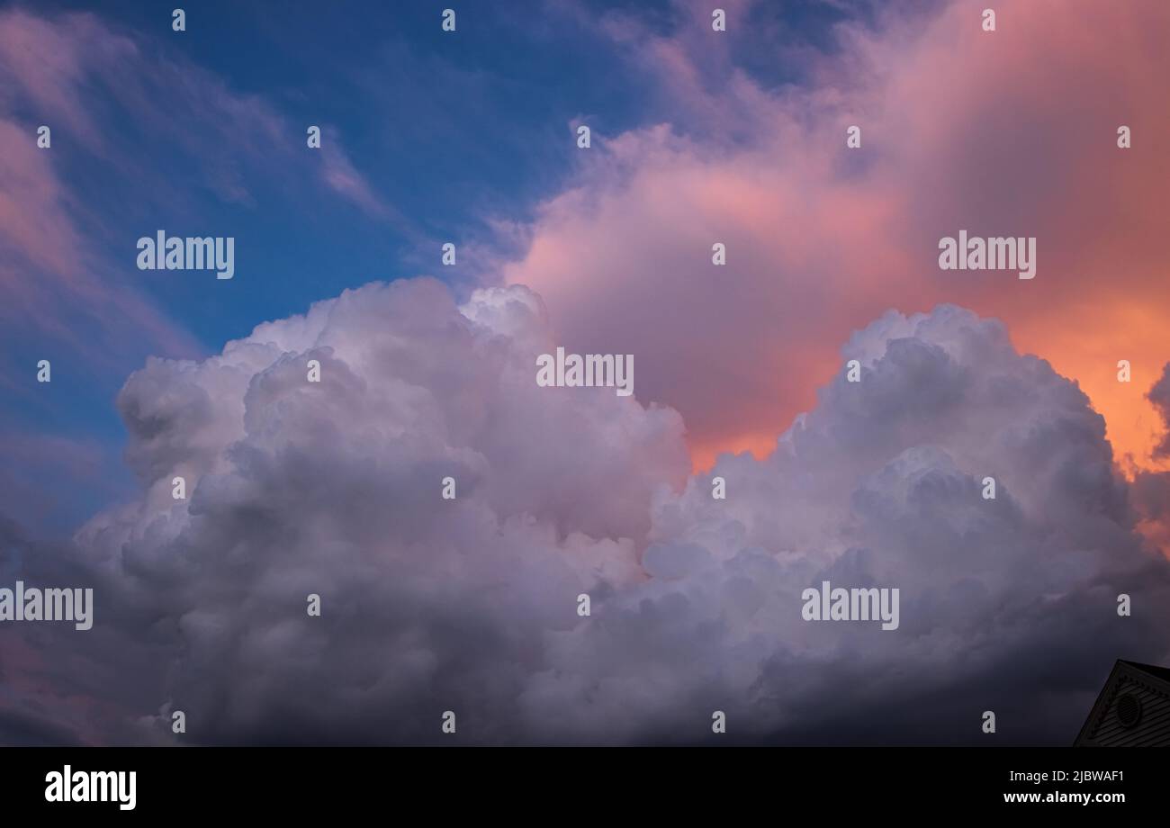 Dramatic and detailed cumulus clouds piled together on a blue sky with golden and orange light from the sun showing through Stock Photo