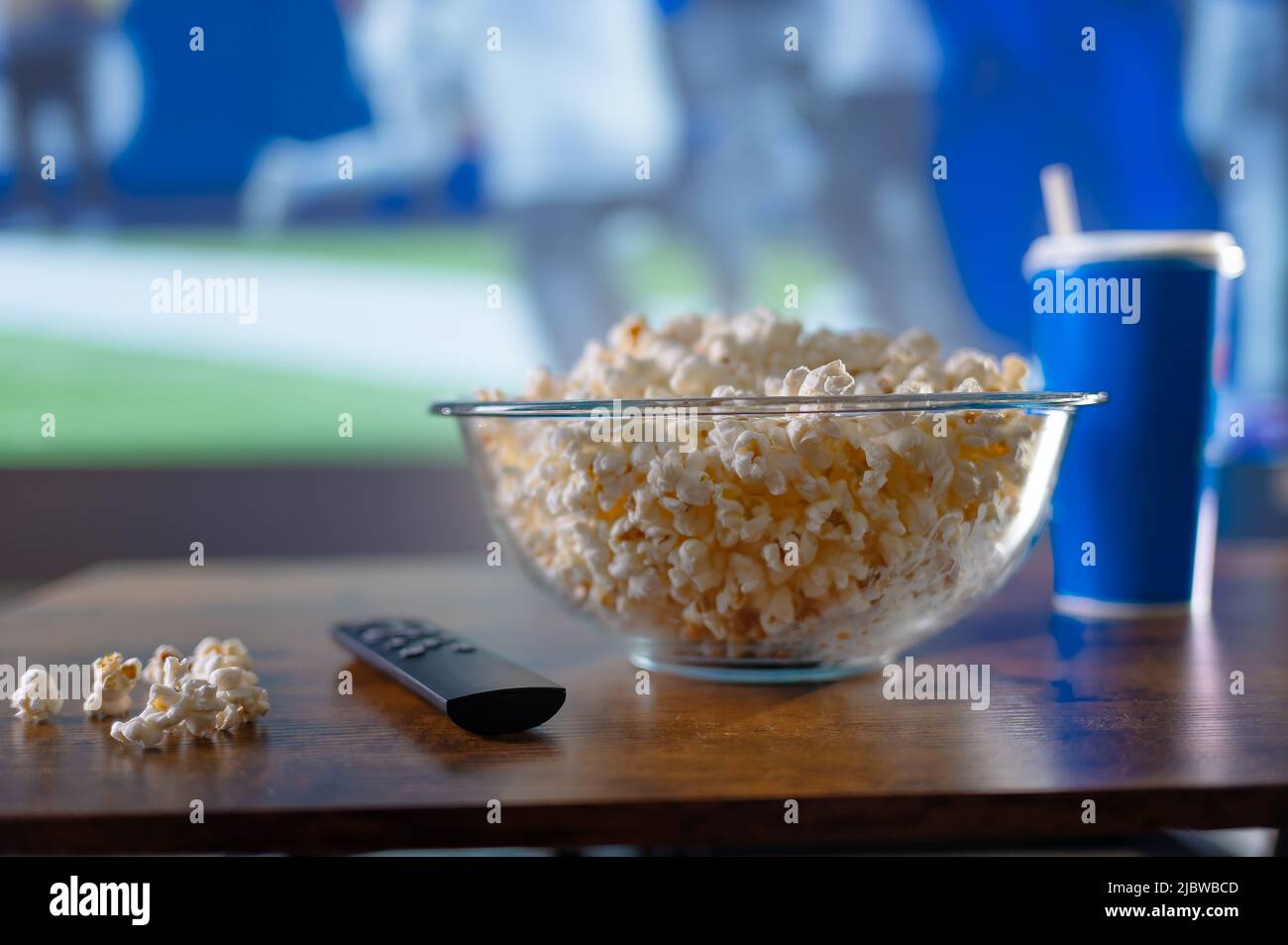 Appetizing popcorn in a glass bowl, TV remote control, drink in a glass ...