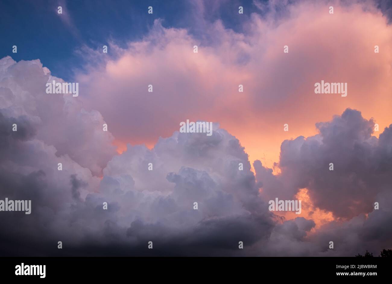 Dramatic and detailed cumulus clouds piled together on a blue sky with golden and orange light from the sun showing through Stock Photo