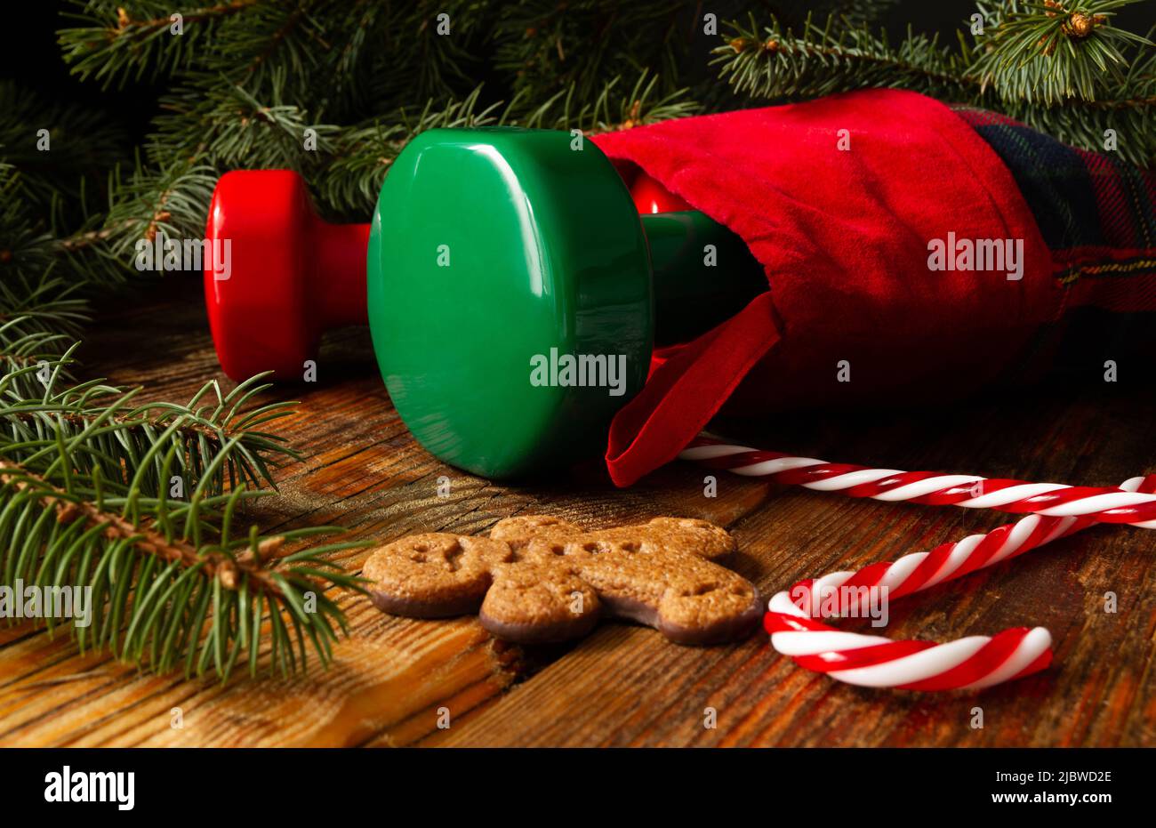 Dumbbells in stocking. Exercise equipment as Christmas gift idea. Gym fitness holiday composition, with gingerbread man cookie, candy cane, tree. Stock Photo