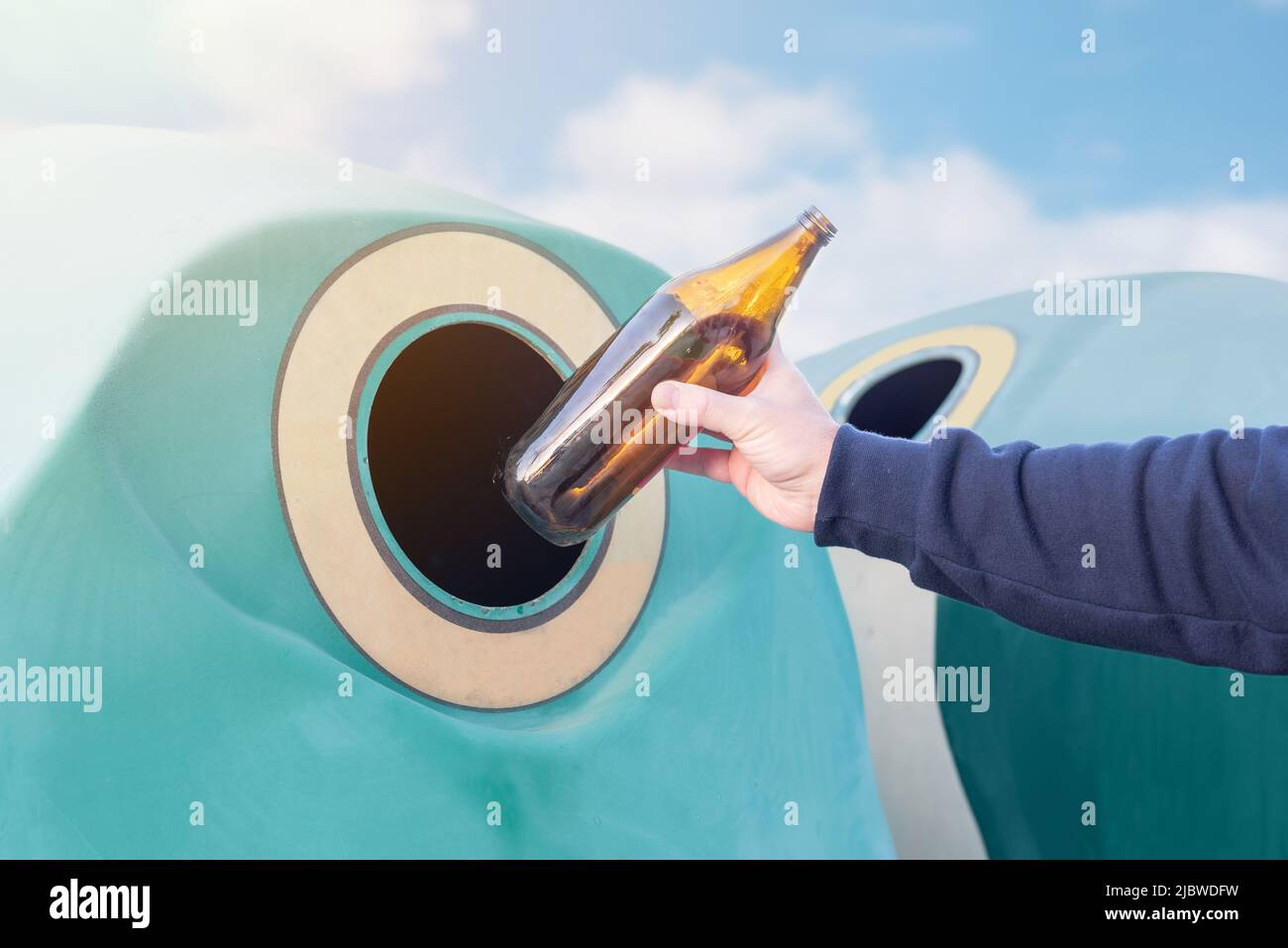 Man recycling glass. Throwing a glass bottle into a green recycling