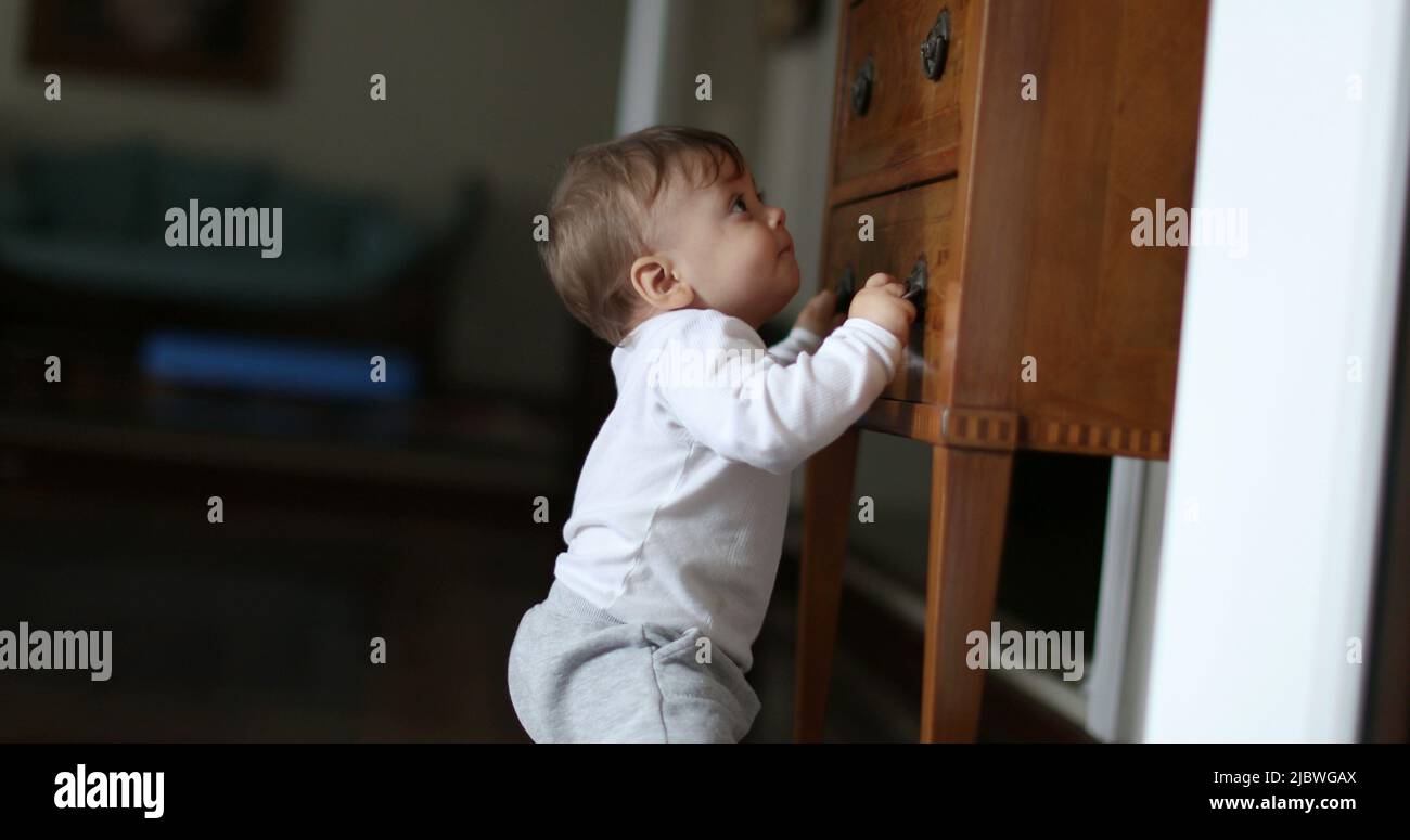 Baby learning to stand by holding into home furniture. Infant toddler
