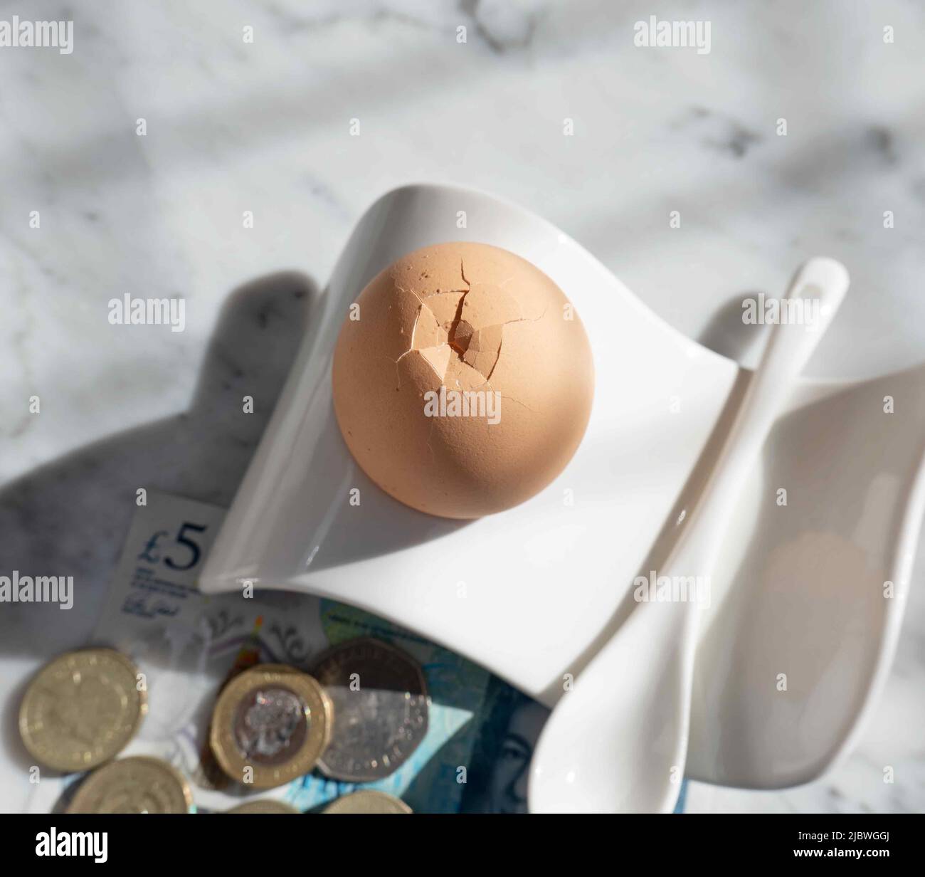 Boiled breakfast egg in an egg cup, five pound banknote and small change in the background. Stock Photo