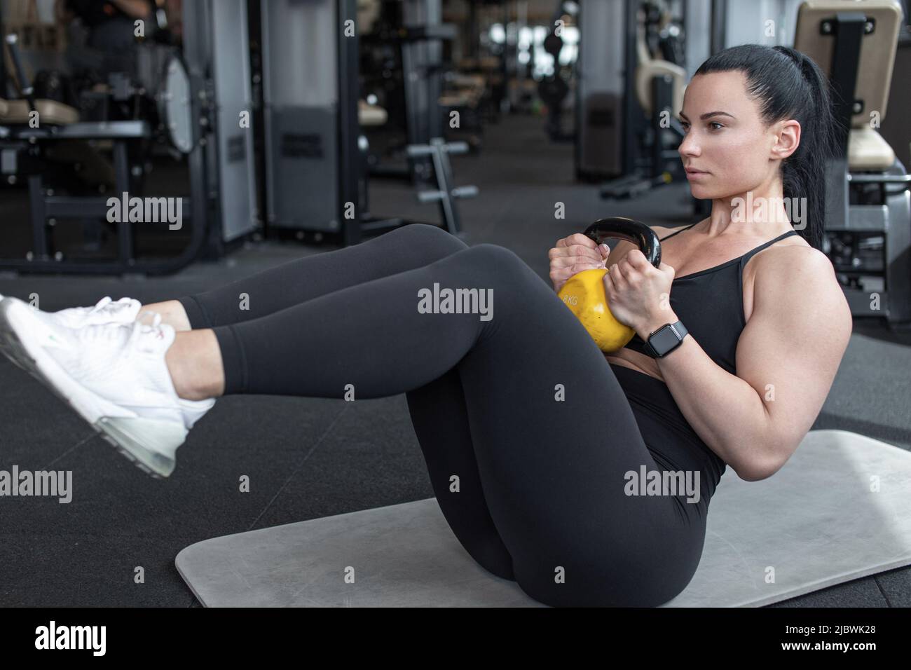 Young woman doing abs workout by kettlebell in gym Stock Photo