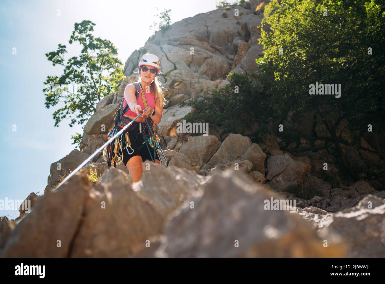 Smiling athletic woman in protective helmet and climbing harness pulling the climbing rope on cliff rock wall in Paklenica National park site in Croat Stock Photo