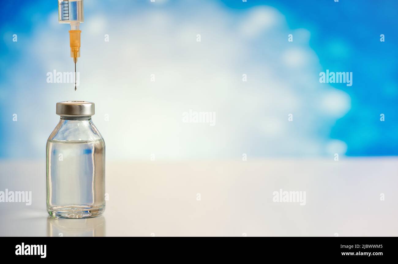 Injection syringe needle with drop of liquid above clear glass vaccine bottle without label, closeup detail space for text right side Stock Photo