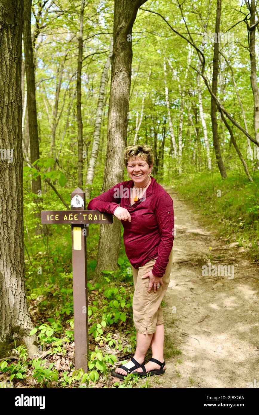 Woman hiker standing and leaning on trail sign marking pathway into forest for Ice Age National Scenic Trail, Elkhart Lake, Wisconsin, USA Stock Photo