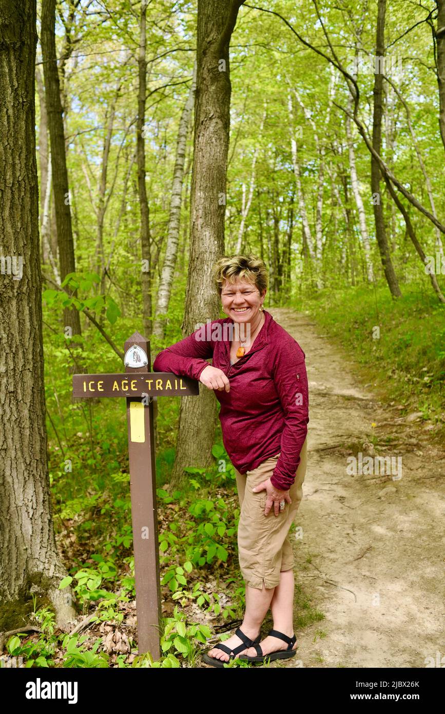 Woman hiker standing and leaning on trail sign marking pathway into forest for Ice Age National Scenic Trail, Elkhart Lake, Wisconsin, USA Stock Photo