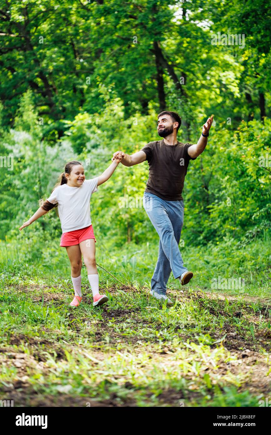 Portrait of smiling family walking pacing in forest around trees, having fun. Little girl holding hand of happy father. Stock Photo
