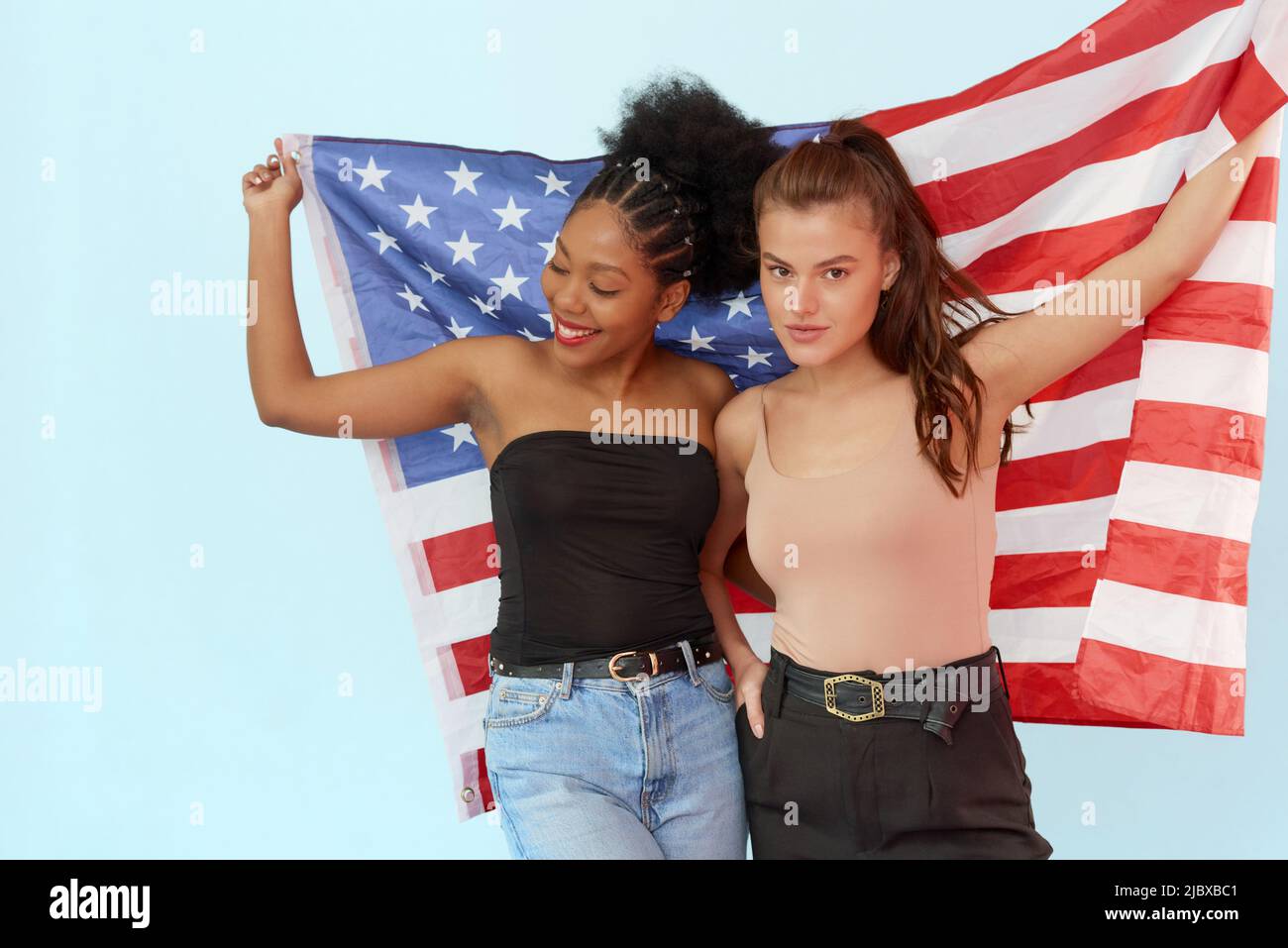 The concept of the unity of different nations and independence day of the usa - july 4. African american woman and caucasian woman holding usa flag in Stock Photo