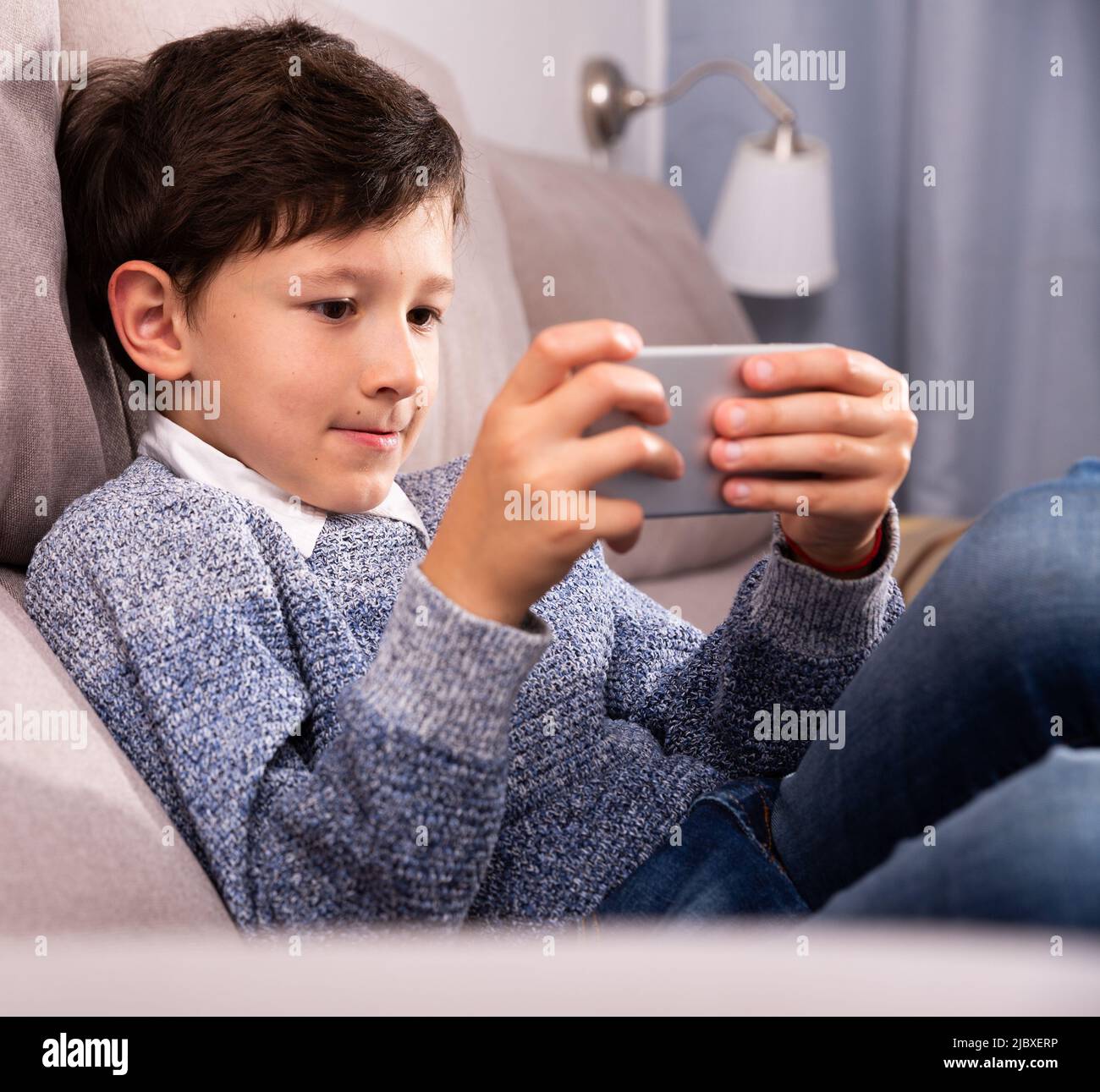 Teenager plays on smartphone in home interior Stock Photo