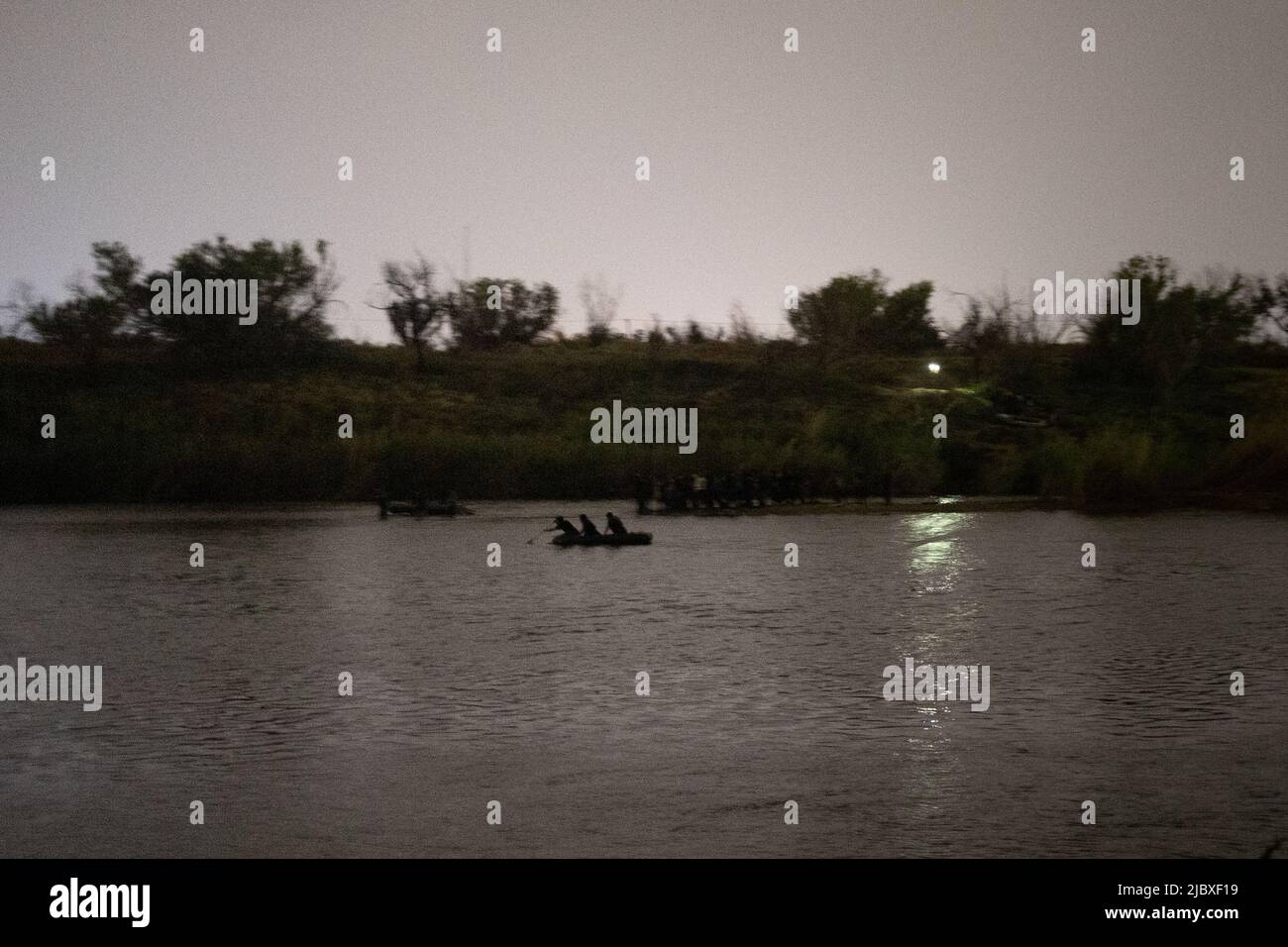 Smugglers paddle past asylum seeking migrants standing on a sandbar as they prepare to cross the Rio Grande river into the United States from Mexico as photographed from Roma, Texas, June 8, 2022.  REUTERS/Adrees Latif Stock Photo