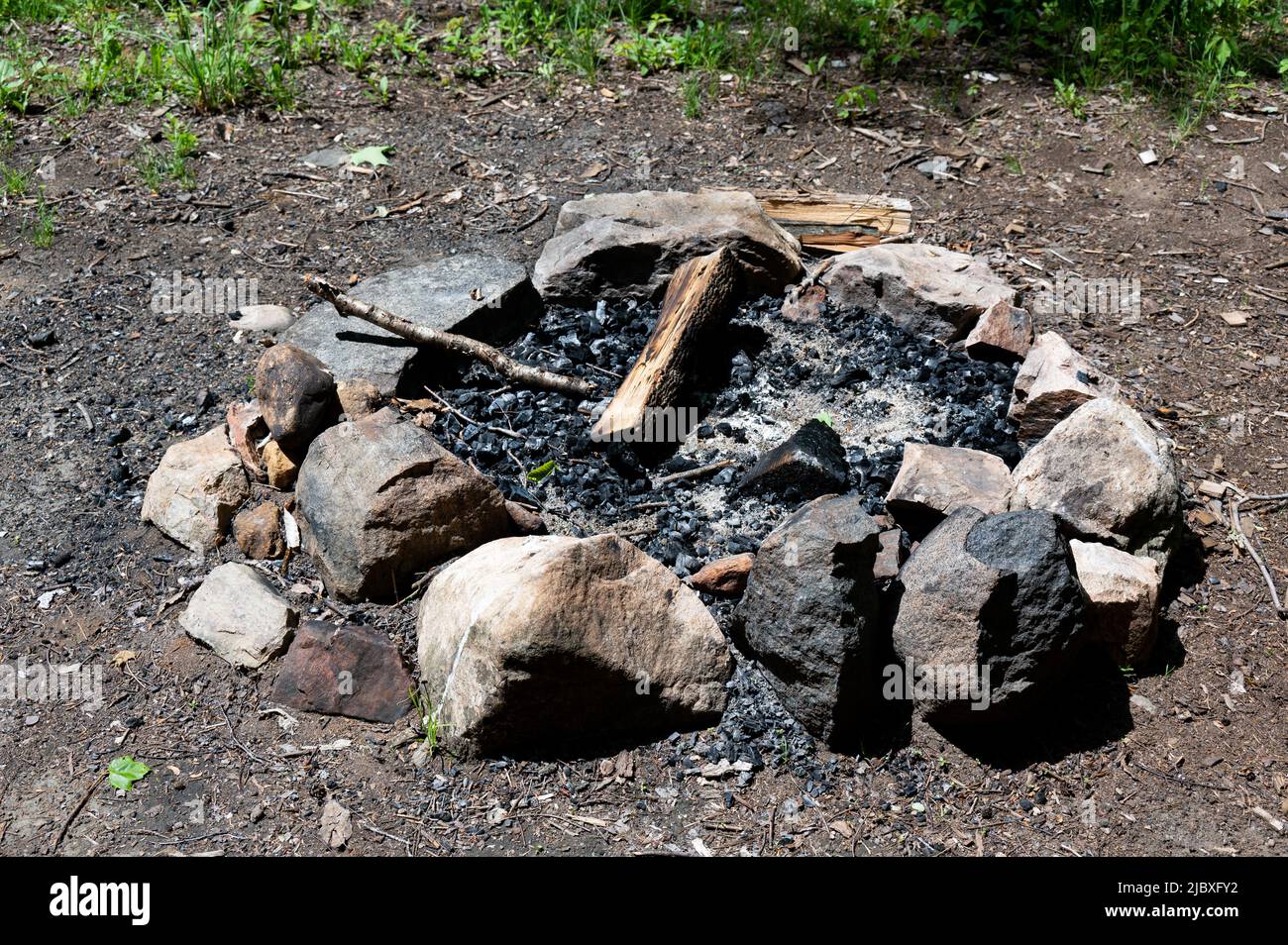 A. stone fire ring with ashes and unburned fire wood at a primitive campsite in the Adirondack Mountains, NY USA wilderness Stock Photo