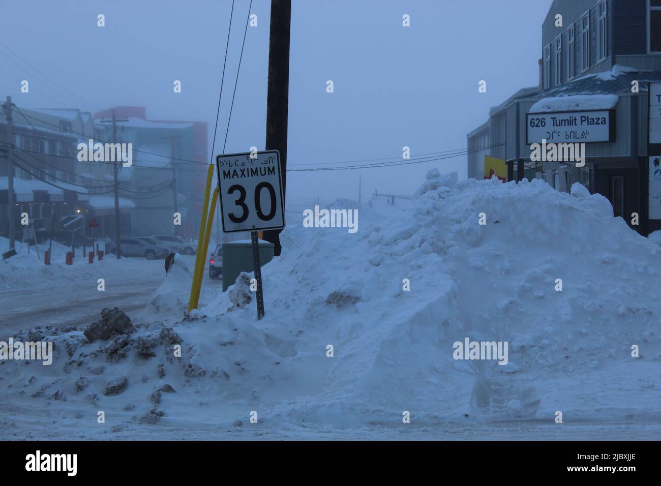 Road sign and snow dump In Iqaluit, Nunavut, Canada on a cloudy day Stock Photo