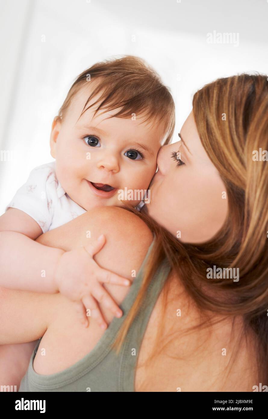 Mother holding baby daughter and kissing her on the cheek Stock Photo