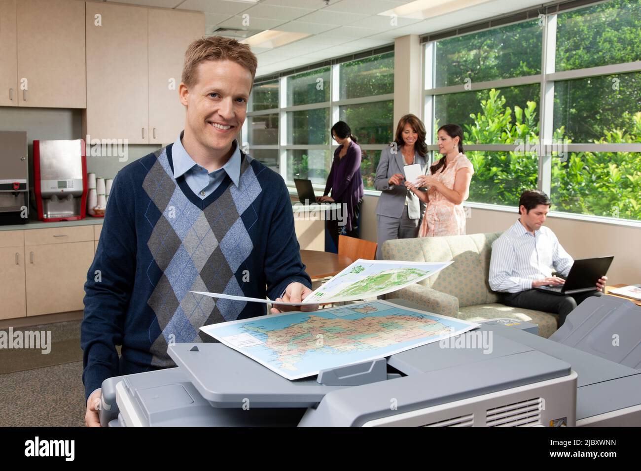 Portrait of a Caucasian man standing at a printer while in breakroom. Stock Photo