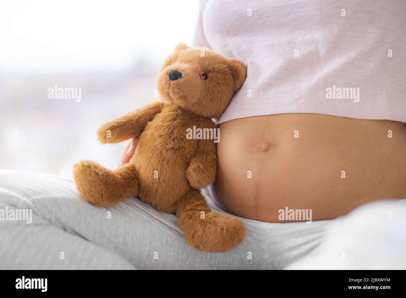 Pregnant woman belly closeup with baby toy teddy bear plush. Skincare, stretch mark, common skin problems of pregnancy. Healthy expecting girl Stock Photo