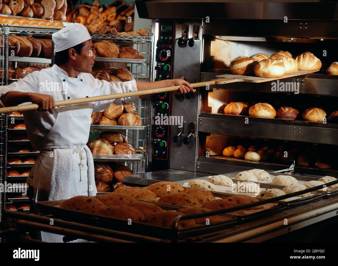 Baker feeding loafs of dough into industrial bakery oven Stock Photo