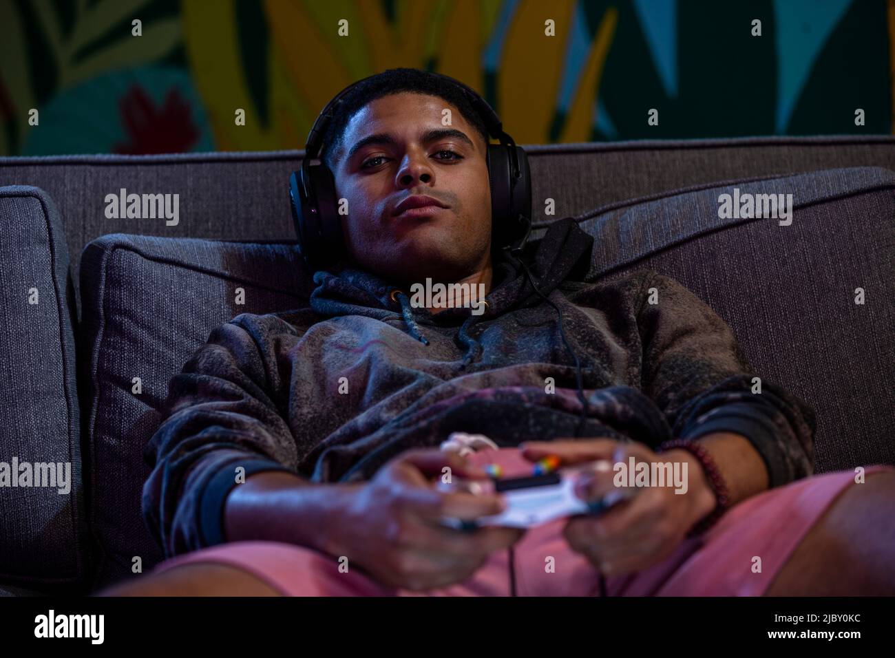 Young man laying back on sofa with video game controller in hand and headset Stock Photo