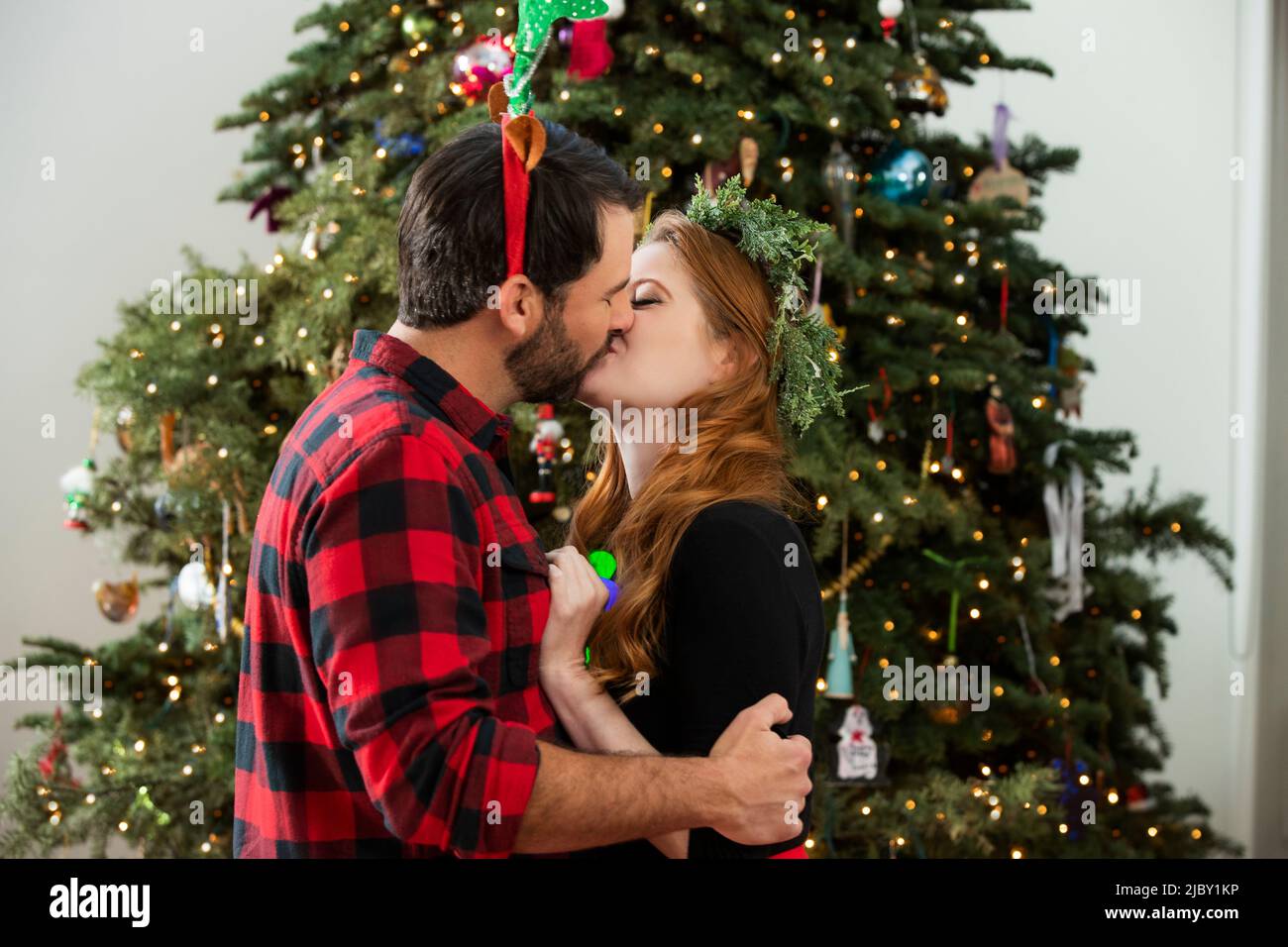 Affectionate young couple kissing under Christmas tree. Stock Photo