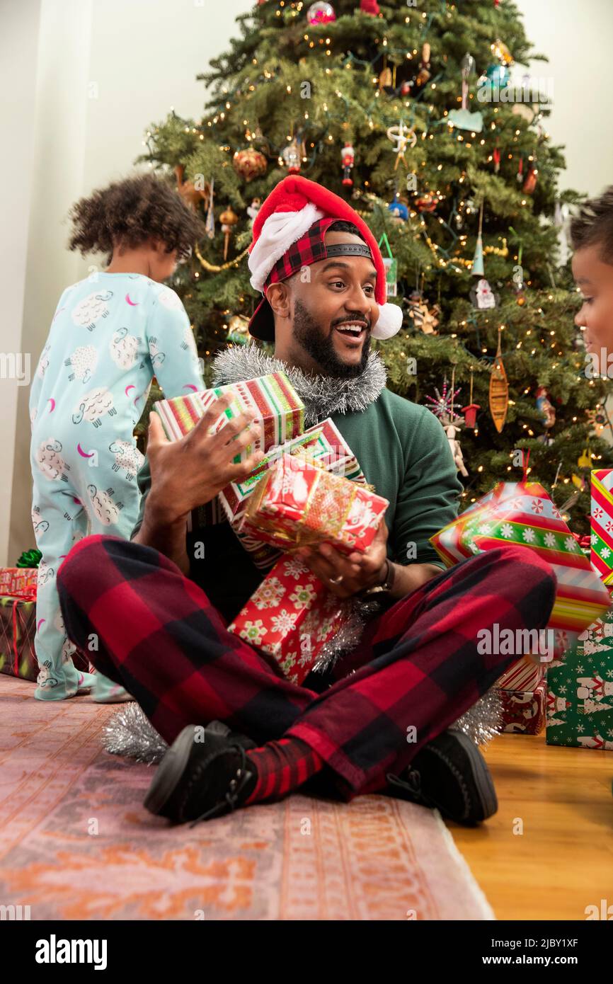 Kids piling up presents on theirs father's lap on Christmas Eve. Stock Photo