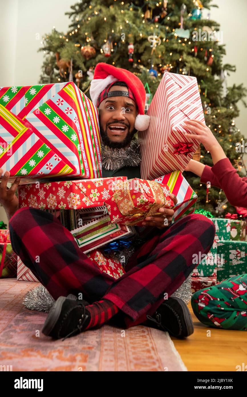 Goofy looking father with concerned expression as kids stack presents on him. Stock Photo