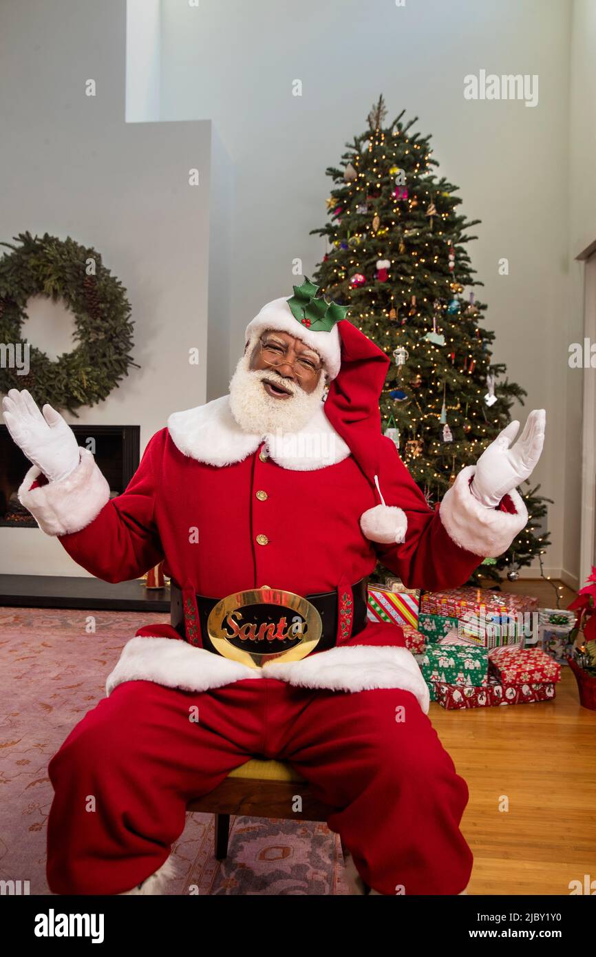A very merry Black Santa Claus looking into camera smiling with his arms outstretched by his side. Stock Photo