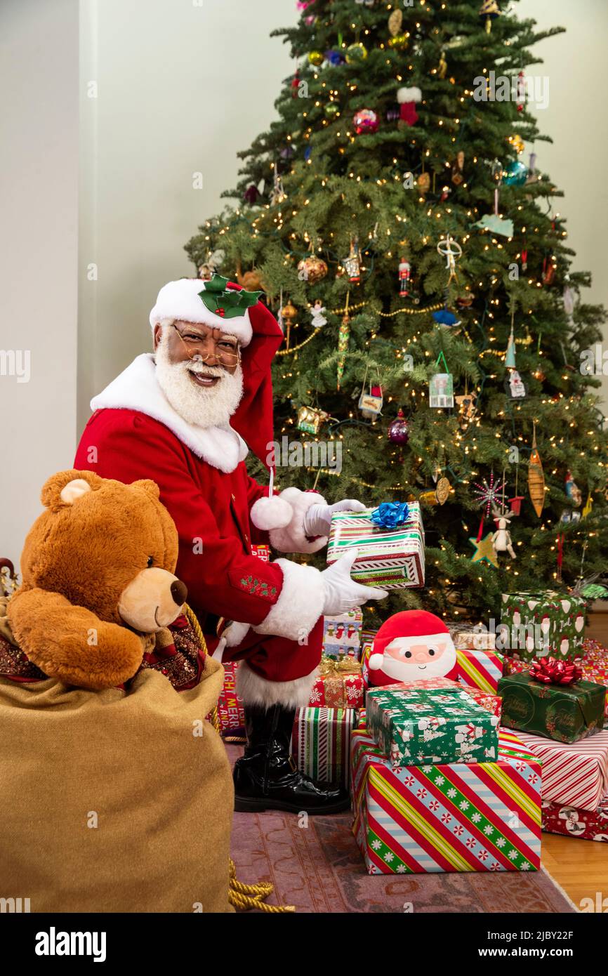 Portrait of Santa Claus under Christmas tree dropping off presents with large toy sack sitting next to him. Stock Photo