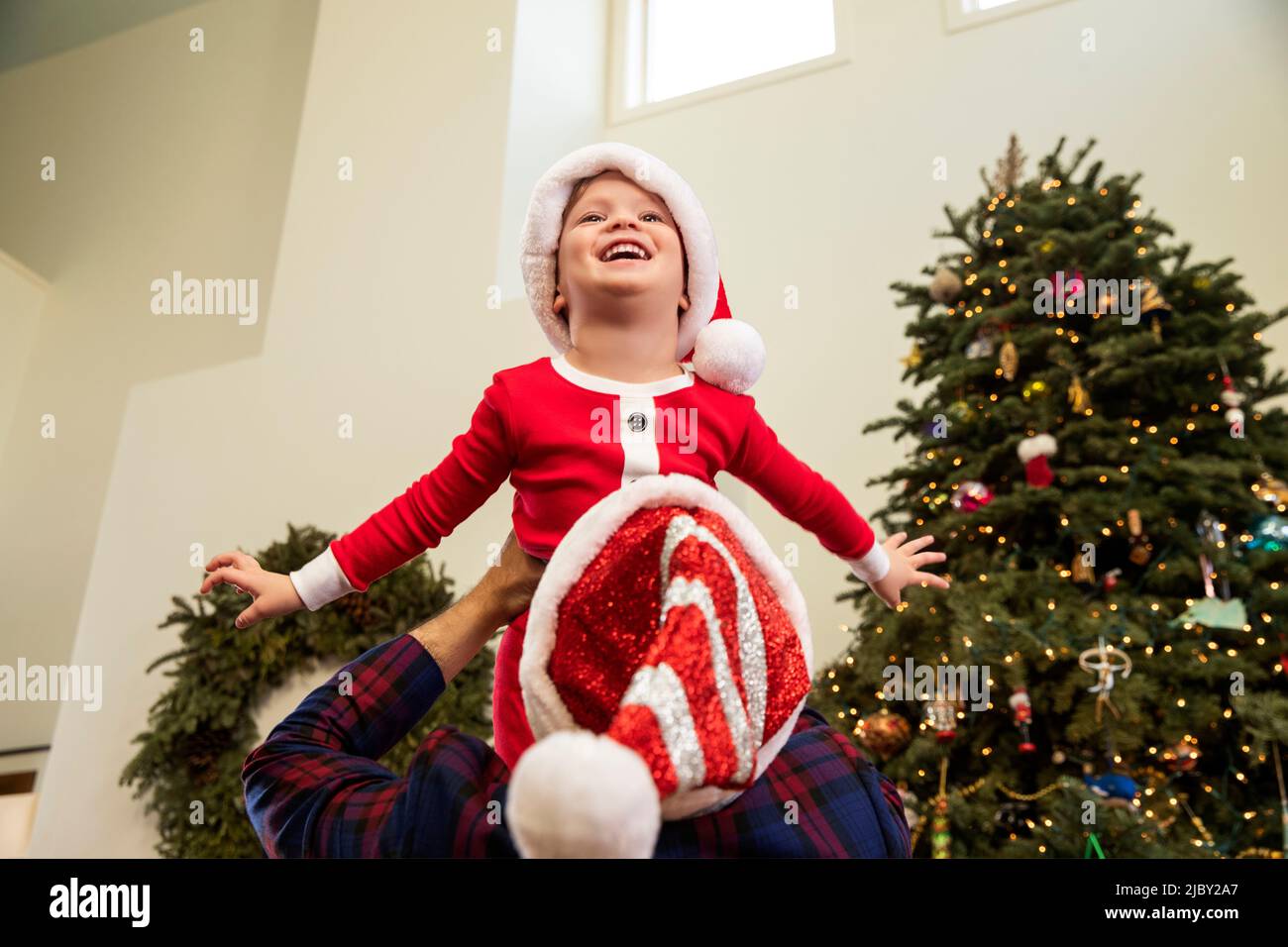 Boy wearing Santa hat being lifted up over his fathers shoulders Stock Photo