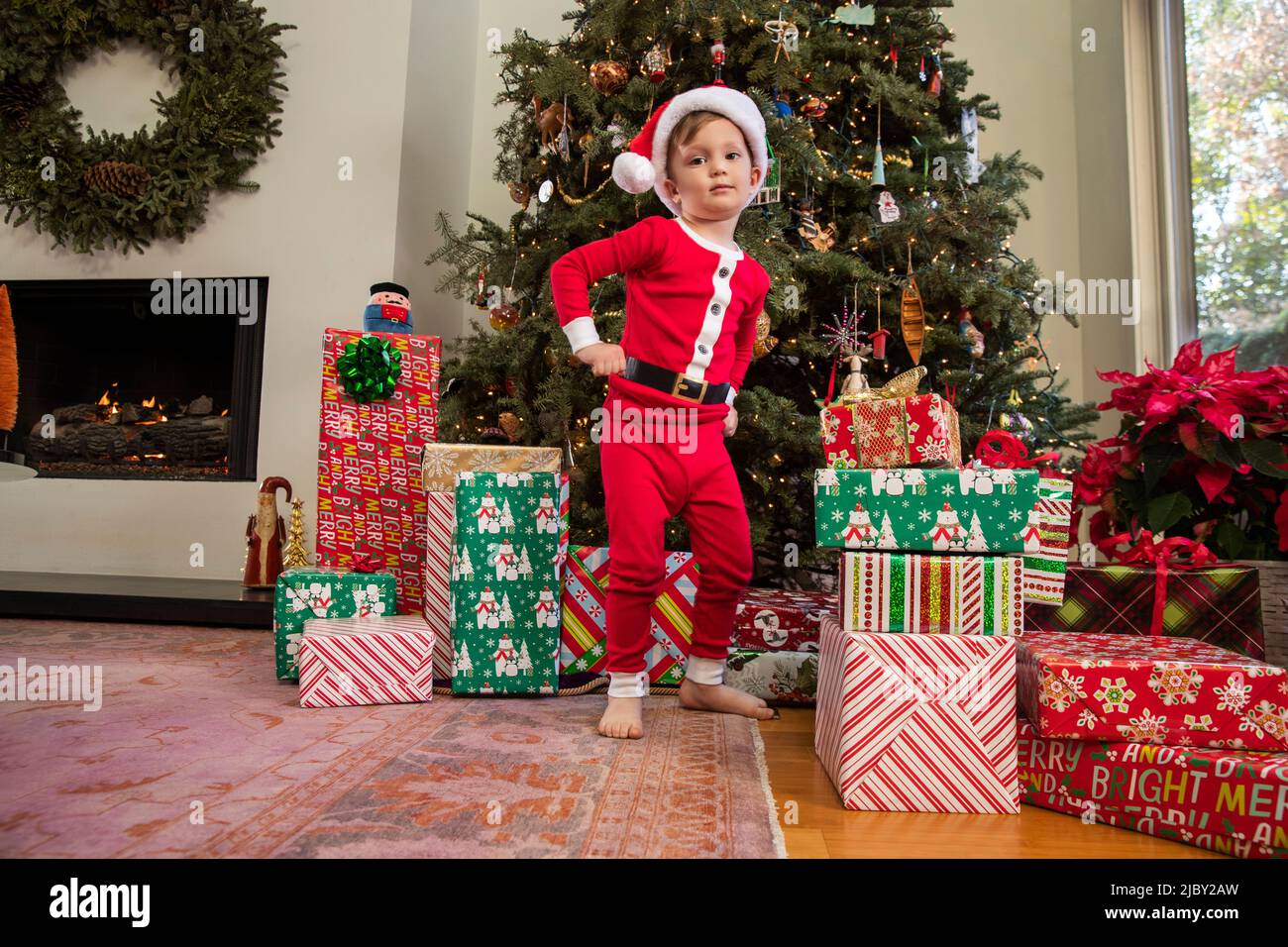 Portrait of a young boy dressed up in Santa Claus pajamas and a Santa hat  standing in front of Christmas tree Stock Photo - Alamy