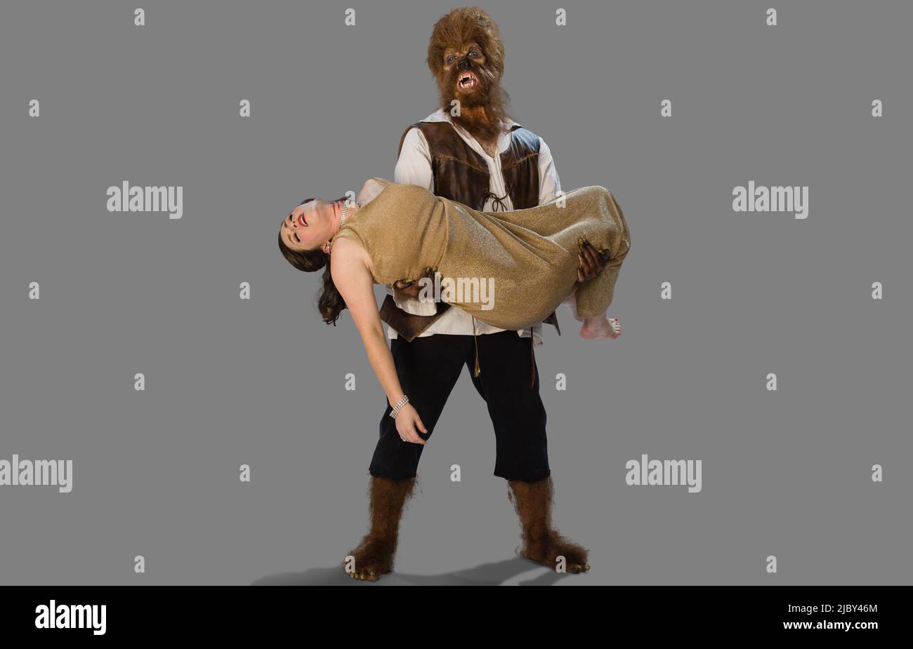 wolf holding a dead woman and lover, in his arms with a distraught and sad expression on his face, two people in Halloween costumes on gray background Stock Photo