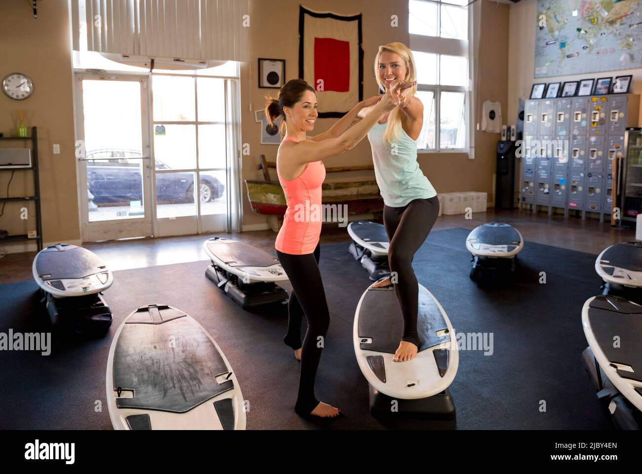 An instructor helping a woman execute a yoga pose on a balance surfboard exercise machine in gym