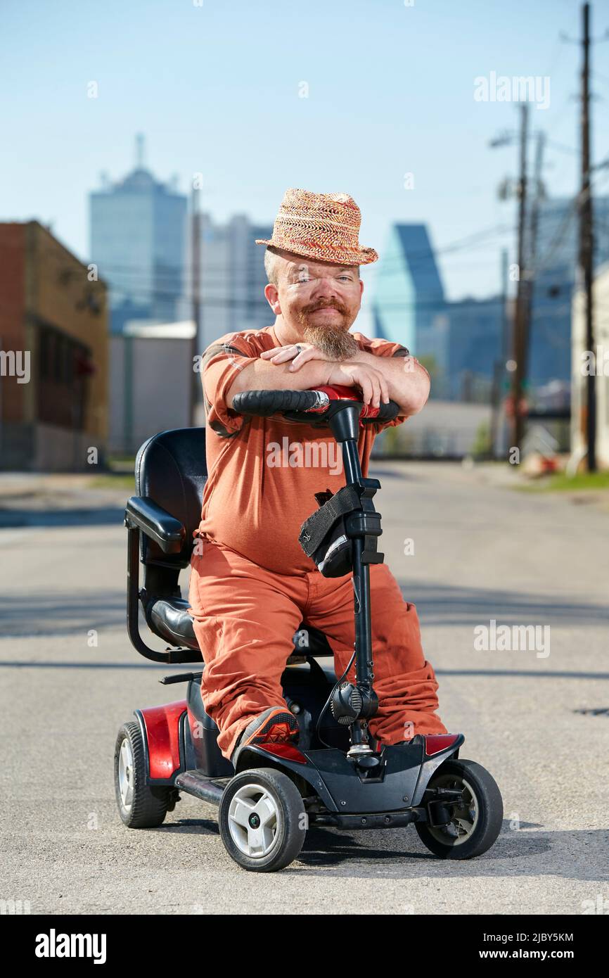 Portrait of male dwarf in sitting on scooter, looking into camera with big smile. Stock Photo