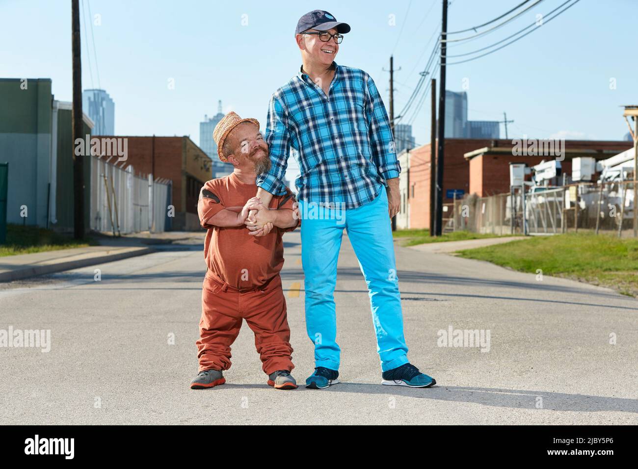 Portrait of male dwarf little person hugging his friend, standing in middle of street. Stock Photo