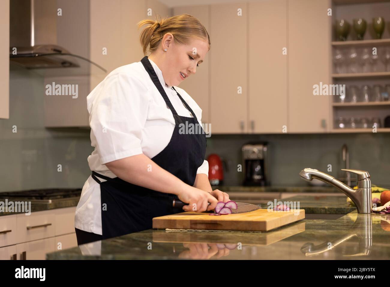 Professional Chef Megan Gill in home kitchen cutting a radish on cutting board Stock Photo