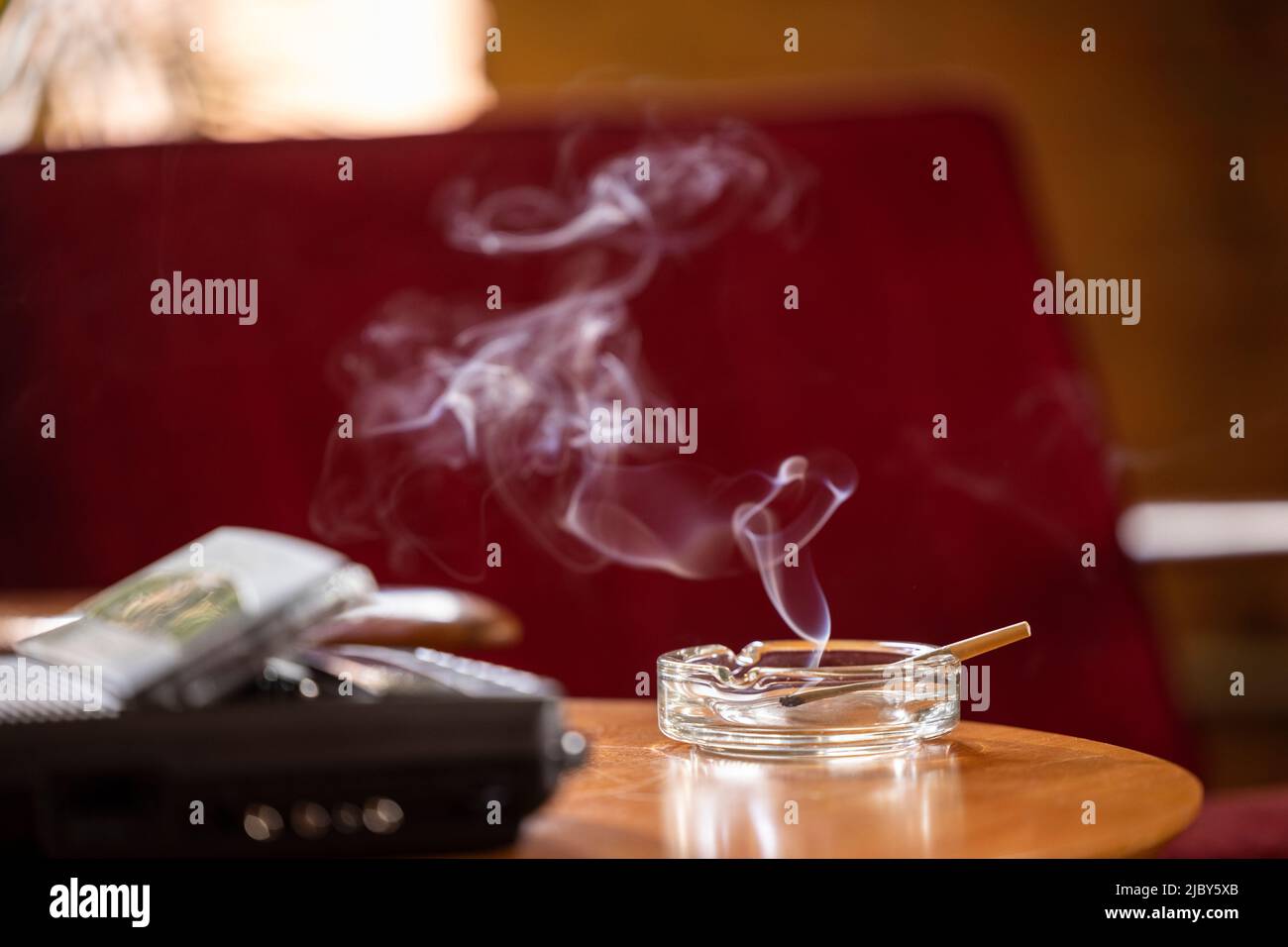 terior, detail of side table with vintage tape recorder / answering machine and ashtray that has a lit CBD pre-roll joint, cigarette with smoke rising Stock Photo