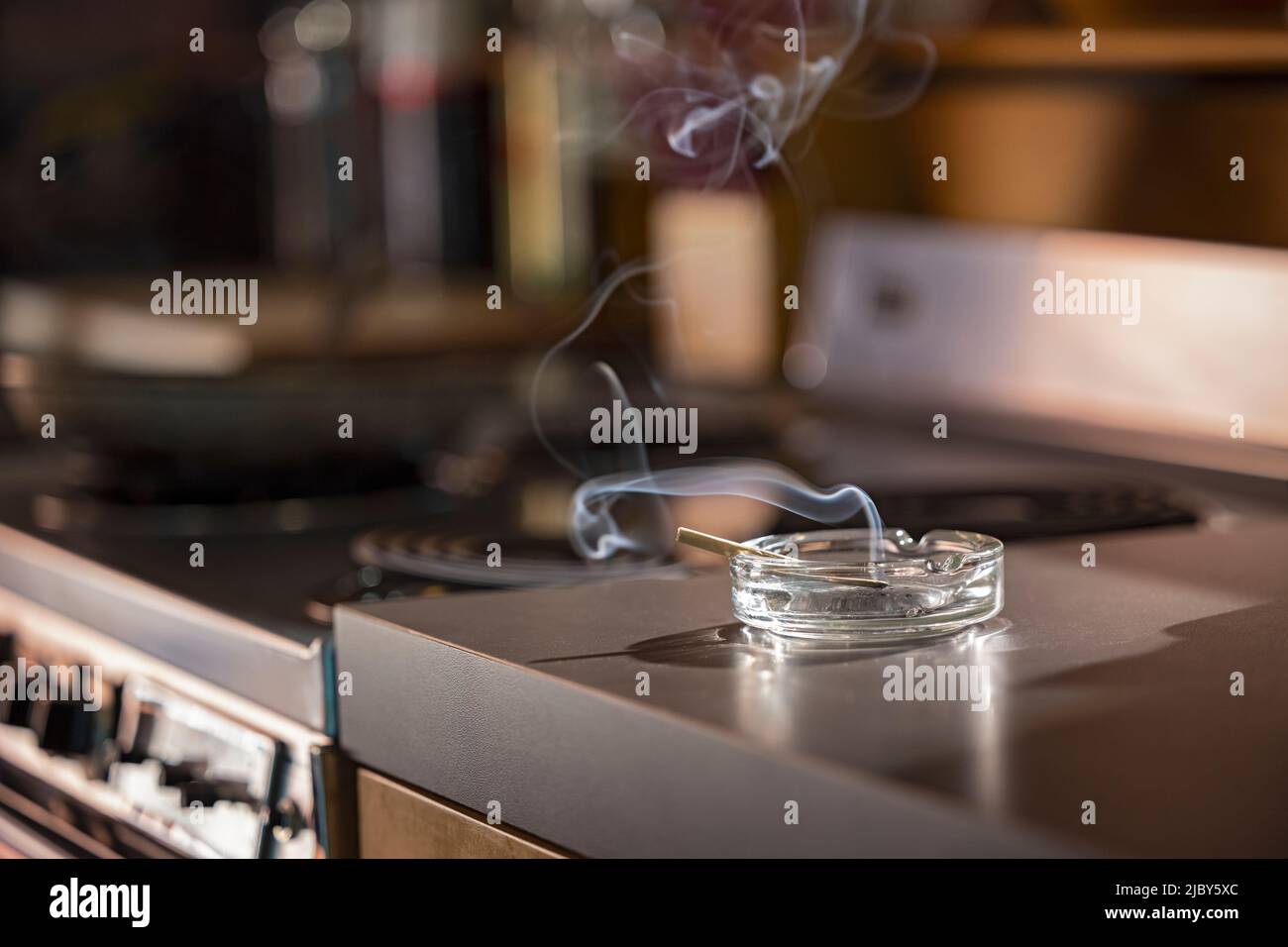 Home Interior, detail of ashtray that has a lit CBD pre-roll joint, cigarette with smoke rising sitting in kitchen next to stove top Stock Photo