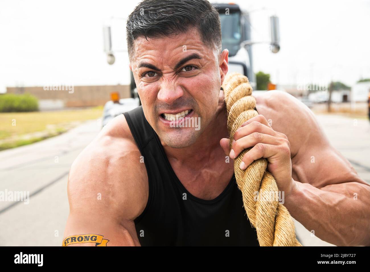 Muscular Hispanic man wearing tank top with “Strong” tattoo on his