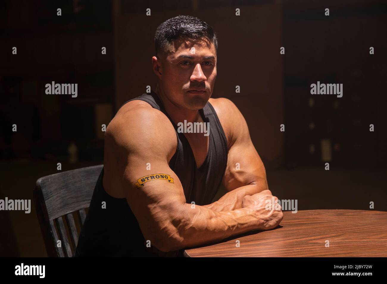 Muscular Hispanic man wearing tank top with “Strong” tattoo on his