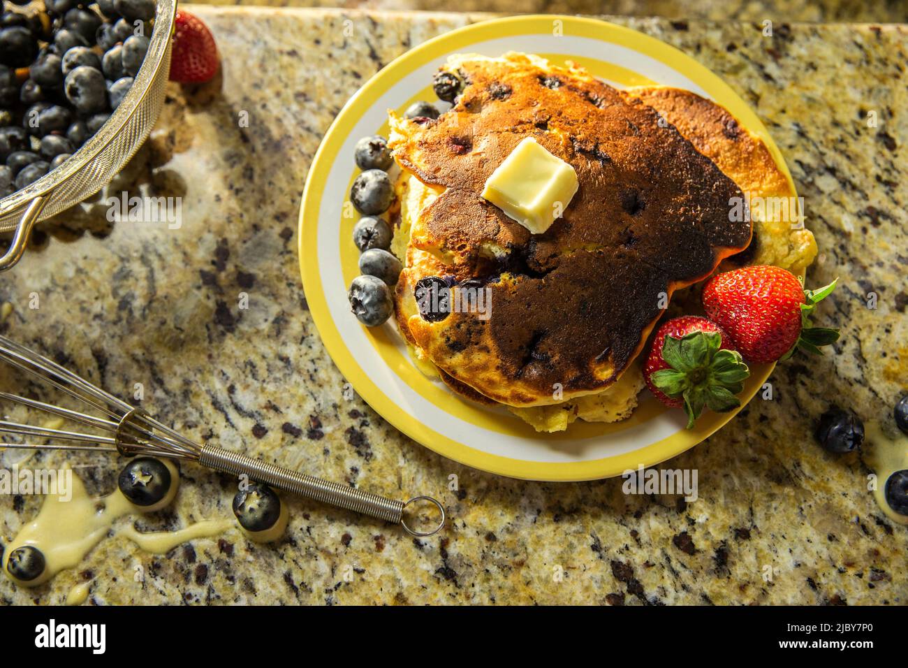 Detail of plate of pancakes with fruit on messy kitchen counter after making blueberry pancakes Stock Photo