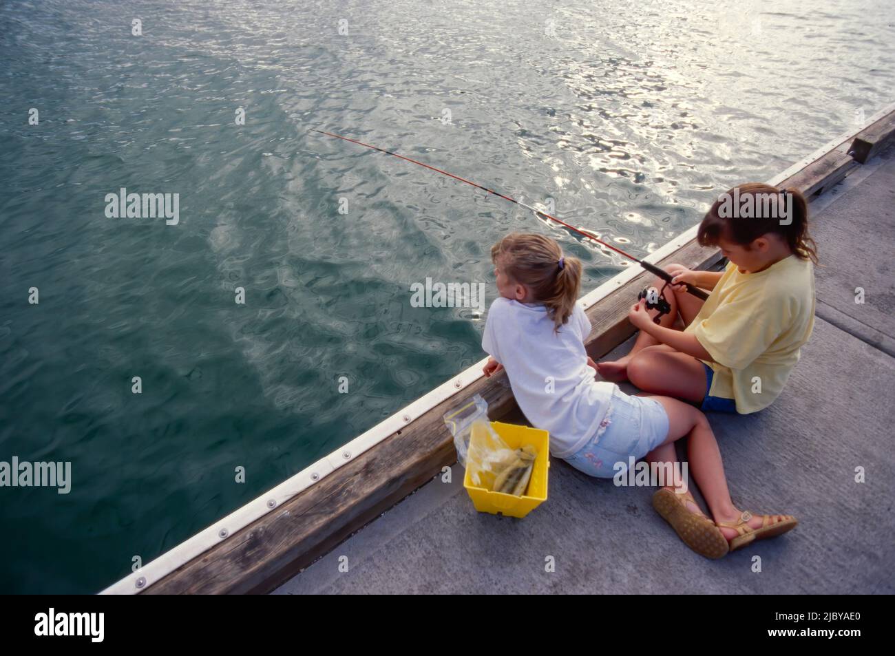 Two young girls fishing off jetty Stock Photo Alamy